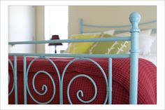 a blue metal bed frame with red blankets and pillows on it's sides, in a bedroom