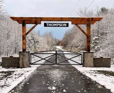 a gate with a sign that says thompson on it in front of snow covered trees