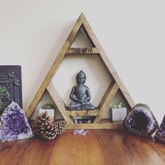 a wooden shelf topped with purple rocks and a buddha statue next to a pine cone