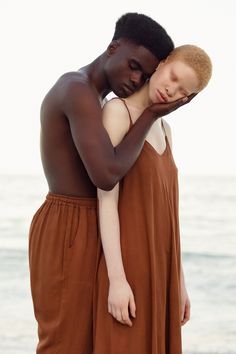 two people standing next to each other near the ocean with their eyes closed and one person covering his face