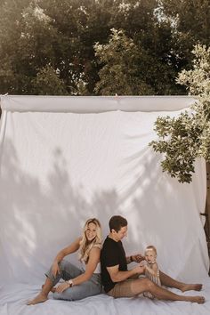 a man and woman are sitting on a bed with a baby in front of them