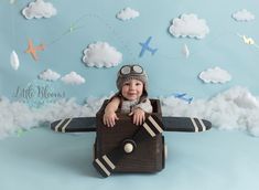 a baby sitting on top of a wooden plane in front of a blue background with clouds