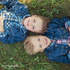 two young boys laying on the ground in front of some green grass and plants with their arms around each other