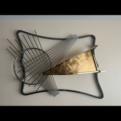 a metal sculpture with some gold and silver items on it's sides, hanging from the wall