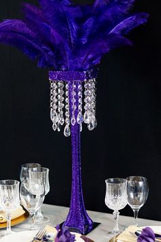 a purple vase with feathers on top of it and wine glasses in front of it