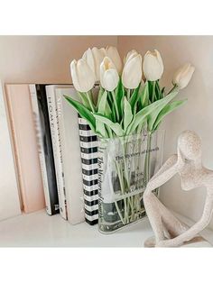 a vase filled with white tulips sitting on top of a table next to a book