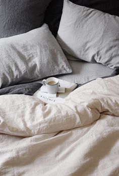 an unmade bed with two pillows and a cup of coffee on the pillow case