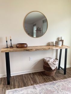 a wooden table with a mirror on the wall above it next to a basket and candles