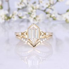 a gold ring with an emerald cut diamond in the center and white flowers behind it