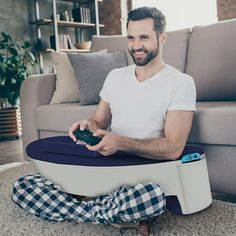 a man sitting on the floor with a remote control in his hand and smiling at the camera