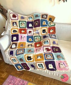 a crocheted blanket with cats on it is sitting on a couch next to a white chair