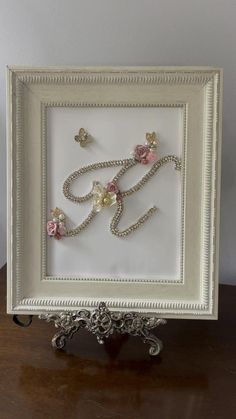 a white frame with beads and flowers in the shape of an e on top of a wooden table