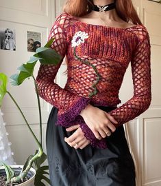 a woman with red hair is standing in front of a potted plant and wearing a crochet top