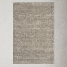 a square rug with squares on it in grey and white colors, against a wall