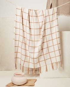 a white vase sitting on top of a wooden table next to a plaid blanket hanging from a clothes line