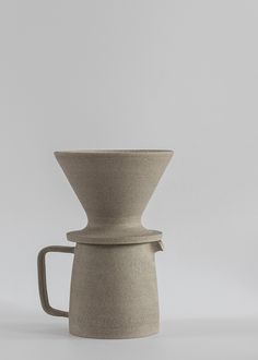 a white coffee cup with a handle on the top and bottom, sitting in front of a gray background