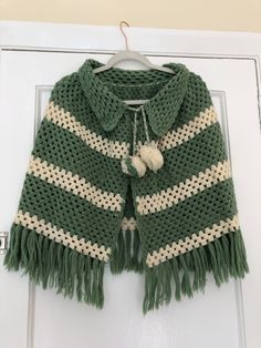 a green and white knitted ponchy hanging on a door handle with tassels