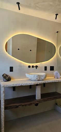 a bathroom with two sinks and a large oval mirror above the sink is illuminated by lights