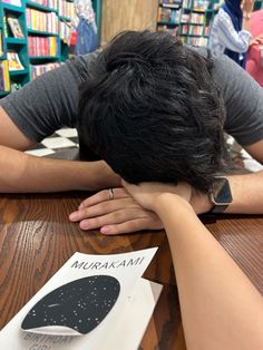 a person sitting at a table with their head on his hands, in front of bookshelves