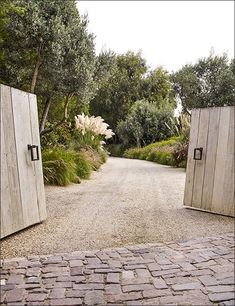 two wooden doors are open on a cobblestone road in front of some trees