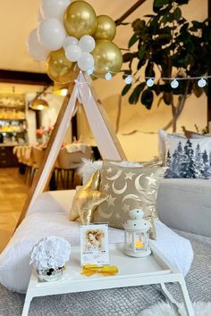 a white table topped with balloons next to a bed covered in blankets and throw pillows