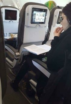 a woman is sitting on an airplane with her headphones up to her ear and looking at the screen