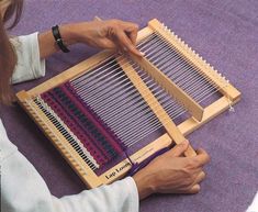 a woman sitting on the floor working with an old weaving loom in her hands