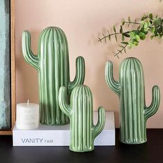 three green cactus statues sitting on top of a shelf next to a candle and plant