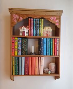 a wooden shelf filled with lots of books next to a wall mounted candle and vase