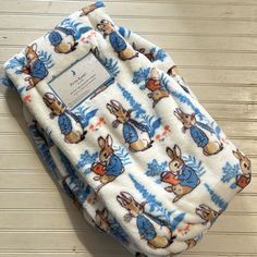 a blue and white blanket with peter rabbit on it's side sitting on a wooden floor