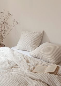 a bed with two pillows and a book on top of it next to a plant