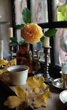 a table topped with flowers and candles next to a vase filled with leaves on top of it