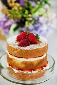 a three layer cake with strawberries on top and flowers in the backgroud