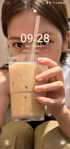 a woman holding up a drink in front of her face with the time displayed on it