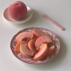 a plate with sliced peaches on it next to a fork and bowl of fruit