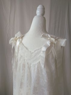 Vintage white lace and ribbon nightgown by Aristocraft. Features sheer lace overlay against nylon lining, standard sleeveless straps decorated with satin bows on the back of the straps, decorative satin ribbon accents placed vertically across the front, and satin bows across the lightly ruffled hem. Straps are not adjustable. Era: Circa 1960s Condition: Excellent Size: Small Color: White Brand: Aristocraft Measurements: 20.5in pit to pit, 38.5in length Fabric Content: 100% nylon Shown on a mannequin with a 33" bust, 26" waist, and 35" hips. Fits a size 2-4. Model is 5'5 with a 34A bust. Some garments may be clipped onto mannequin or model for display. MORE INFO: *Please, note that these items are vintage. Therefore, it is expected to find some wear. Ariessence by Ariel is an admirer of fas White Lace Nightgown For Wedding, White Lace Wedding Nightgown, Cream Lace Wedding Nightgown, Wedding Cream Lace Nightgown, Cream Lace-trim Sleepwear For Wedding, Cream Wedding Sleepwear With Lace Trim, White Lace Nightgown For Wedding Night, Feminine Wedding Nightgown With Lace Patchwork, White Lace Nightgown With Lace Trim