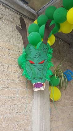 a green dragon mask hanging from the side of a building next to balloons and air plants