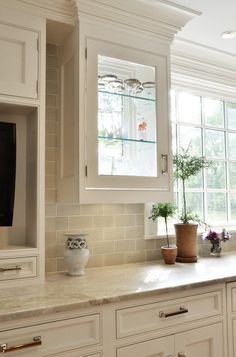 a kitchen with white cabinetry and marble counter tops, along with a television mounted on the wall