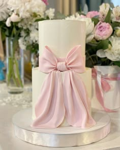 a white and pink wedding cake with a large bow on the top, surrounded by flowers