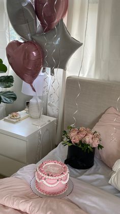 a bed with pink and silver balloons on top of it next to a birthday cake