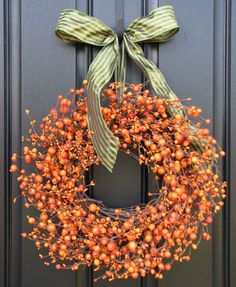 a wreath on the front door is adorned with orange berries and green ribbon, as well as a bow