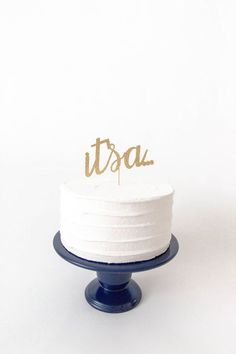 a white cake with gold lettering on top sitting on a blue plate against a white background