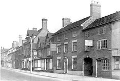 an old black and white photo of buildings on the side of a street in england