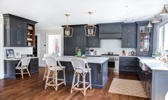 a large kitchen with gray cabinets and white counter tops, wooden flooring and bar stools