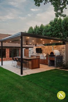 an outdoor kitchen and grill area in a backyard with grass, trees, and brick walls