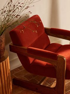 a red chair sitting next to a plant in a vase on top of a wooden table