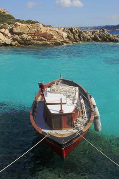 a small boat tied up to the shore in clear blue water with rocks in the background