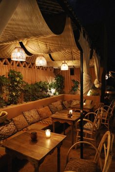 an outdoor seating area at night with lit candles on the tables and plants in pots