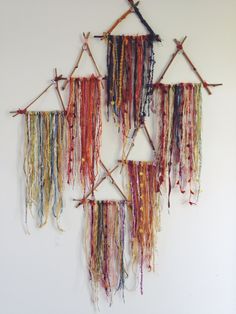 three pieces of art made from yarn hanging on a wall with sticks attached to them