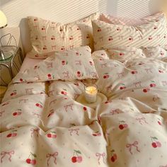 an unmade bed with cherries on it and a lit candle in the middle